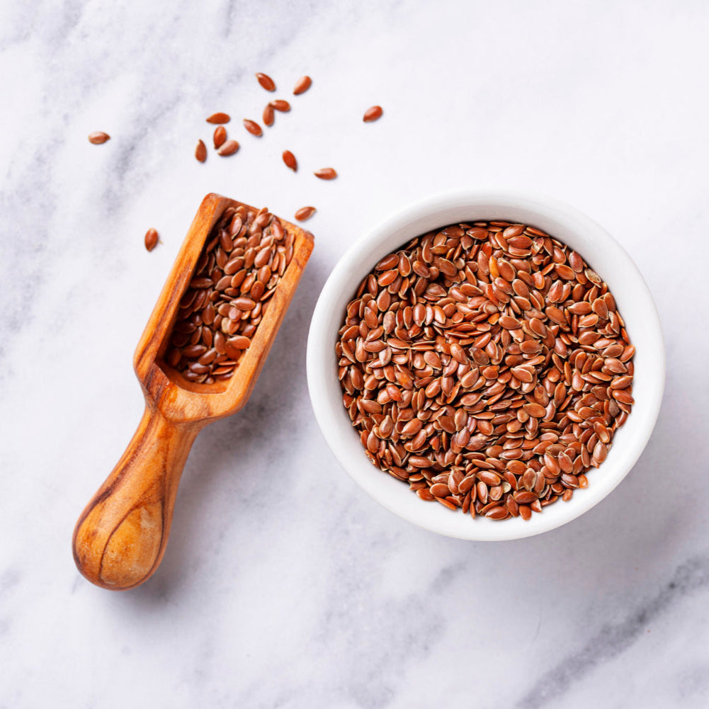 Wooden scoop and bowl filled with flaxseeds on a marble surface