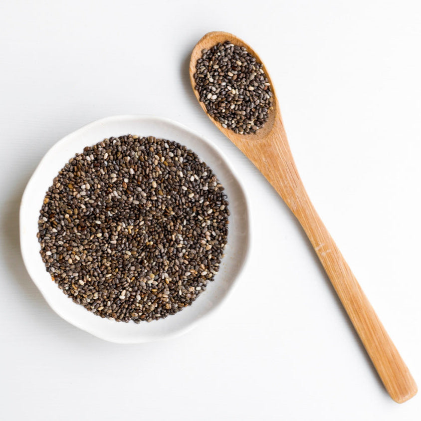 Chia seeds in a white bowl with a wooden spoon on a light background