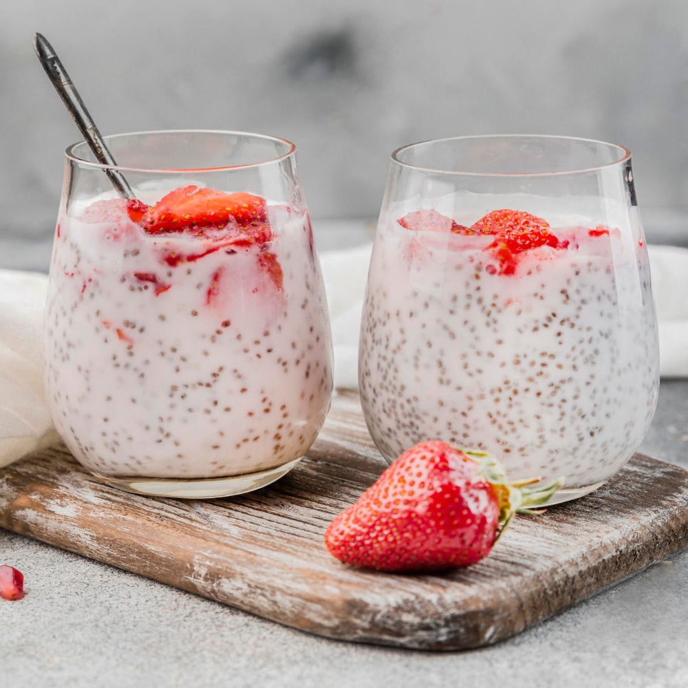 Two glasses of chia pudding with strawberries on a wooden board.