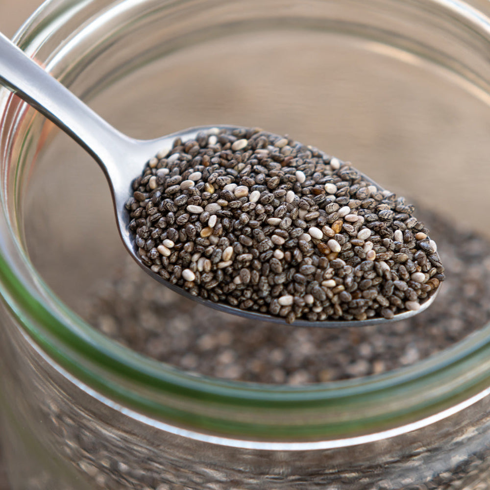 Glass jar filled with chia seeds and a spoonful of seeds above it.